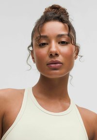 Jasnobeżowy, sportowy top na ramiączkach o dopasowanym kroju i szerokich ramiączkach, wykonany z gładkiego materiału i z minimalną ilością szwów. Brak wzorów i ozdób.