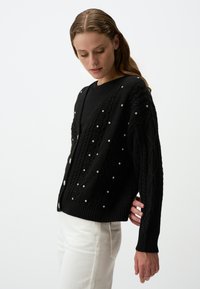 Zwarte gebreide cardigan met een V-hals, met een gewoven patroon en versieringen van kleine, verspreide rhinestones. Ribbelboorden en onderkant.