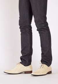 Lace-up schoenen in crèmekleur met bloemenpatroon, met een lage hak en ronde neus, gecombineerd met strakke donkere spijkerbroeken.