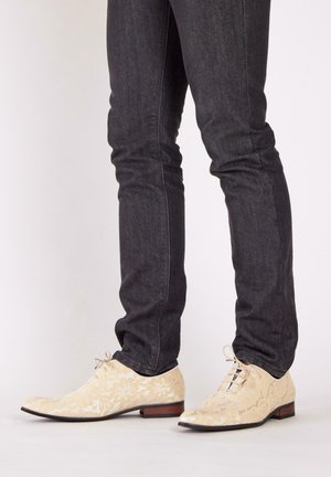 Chaussures à lacets crème avec motif floral, dotées d'un petit talon et d'un bout arrondi, accompagnées d'un jean foncé ajusté.