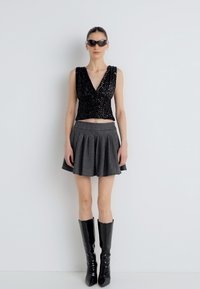 Μαύρο τοπ με παγιέτες, γκρι ριγωτή πλισέ φούστα και μαύρες γυαλιστερές μπότες μέχρι το γόνατο. Το μοντέλο φοράει μαύρα γυαλιά ηλίου.