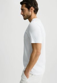 Hvid kortærmet t-shirt i blødt bomuld med rund halsudskæring, glat tekstur og tætsiddende silhuet, bæretsammen med lysebeige bukser.