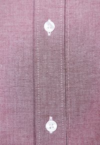 Camicia abbottonata in un tessuto bordeaux texturizzato con un motivo sottile, dotata di bottoni bianchi e cuciture a contrasto lungo la pattina.