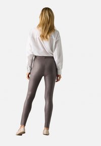 Leggings metálicos grises con una cintura alta y una textura suave, combinados con una camiseta blanca de corte holgado. La figura se muestra de espaldas.