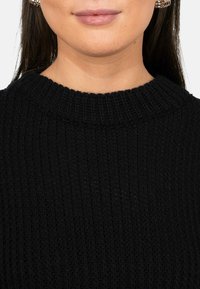 Maglione nero a coste con un collo alto e rotondo. La texture è lavorata e regolarmente patternata, mostrando fine dettagli nella tessitura del tessuto.