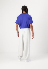 T-shirt bleu à manches courtes associé à un pantalon de jogging gris clair, ample, avec une taille élastique et une poche arrière, porté avec des baskets blanches.