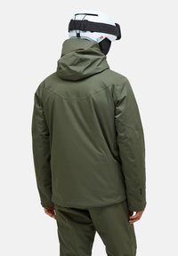 Groene geïsoleerde jas met capuchon, met een sleek, gladde textuur en verstelbare polsmanchetten, gedragen met een witte helm.