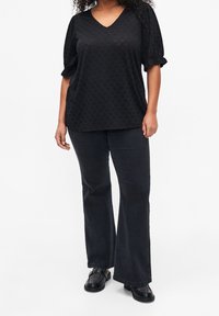 Haut noir à manches courtes avec un décolleté en V et un motif texturé. Associé à un pantalon noir évasé et des chaussures noires perforées.