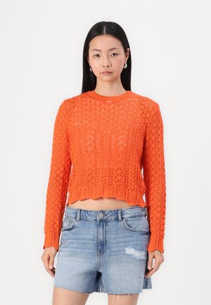 Oranger, gestrickter, verkürzter Pullover mit Rautenmuster und geripptem Saum. Kombiniert mit hellen Denim-Shorts mit einem verwaschenen Finish.