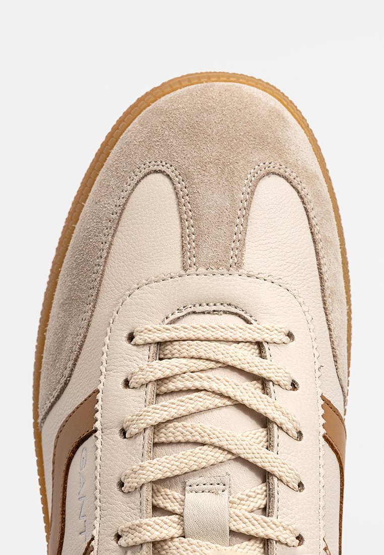 Sneakers in pelle beige con accenti in camoscio, caratterizzati da una superficie testurizzata, punte arrotondate e lacci beige. Dettagli di strisce laterali marroni.