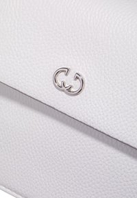 Hvid læder crossbody taske med tekstureret finish. Har et sølvfarvet logo og en klaplukning. Minimalistisk design med slanke kanter.