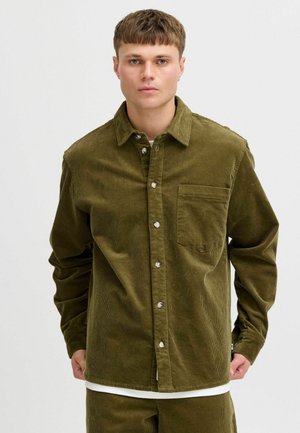 Green corduroy shirt with a button-down style, front pocket, and long sleeves. Features silver buttons and a soft, textured fabric.
