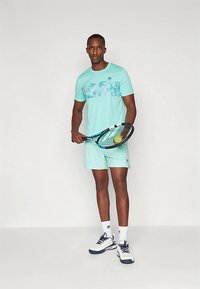 Heledad helesin värvi sportlik riietus, mis koosneb niiskust imavast T-särgist ja lühikesed pükstest, millel on sinine abstraktne muster. Tennise reket koos kollase palliga.