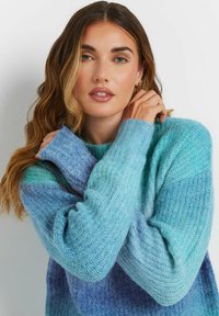 Strickpullover in verschiedenen Tönen von Blau und Türkis, mit lässiger Passform, geripptem Design und breiten Manschetten. Das Material wirkt weich und flauschig.