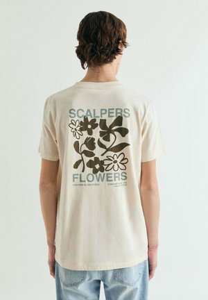 Camiseta beige de algodón con un estampado gráfico floral en verde oscuro en la parte trasera, con los textos "SCALPERS" y "FLOWERS" incluidos.
