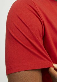 Camiseta de manga corta roja con una textura suave, diseño ajustado y detalles de costura visibles en las mangas y el dobladillo.