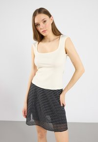 Top de tirantes de canalé en color crema con escote cuadrado, combinado con una falda negra con lunares blancos, de longitud hasta medio muslo y con un tejido vaporoso.