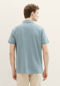 Polo shirt bleu clair à manches courtes avec une texture lisse, doté d'un col classique et d'une fente sur les côtés à l'ourlet pour plus de confort.