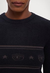 Must mustriga särk, millel on tekstureeritud viimistlus, soonikkoes kaelus ja õrn graafiline muster, kus on kujutatud käsi ja tähti rinna piirkonnas.