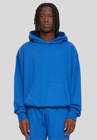 Blauwe hoodie met een ruime voorzak, gemaakt van zacht materiaal, voorzien van een capuchon met trekkoord en een losse pasvorm, aangevuld met bijpassende broeken.