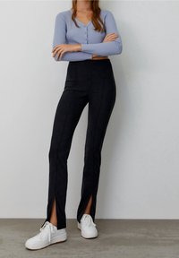 Pantalones negros de cintura alta con aberturas laterales, hechos de un material suave. Combinados con una blusa de manga larga de color azul claro y zapatillas blancas.