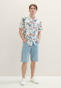 Short-sleeve, button-up shirt with colorful tropical leaf and flower pattern; paired with light blue denim shorts and white sneakers.