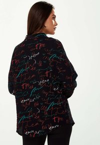 Black textured jacket covered in colorful, abstract handwriting patterns in red, green, and white. Oversized fit with a collar and dropped shoulders.