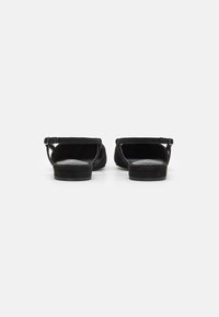 Black suede sandals with a flat sole, open back, and ankle strap. Features smooth texture and minimalistic design.
