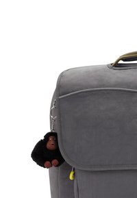 Grauer Rucksack mit strukturiertem Finish, ausgestattet mit einem Klappenverschluss und einem kleinen schwarzen Gorilla-Anhänger, der an einem Zipper hängt.