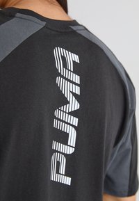 Sort atletisk t-shirt med grå skulderaccenter, der har hvid lodret tekst "PUMP" på ryggen, lavet af et blødt, tekstureret stof.
