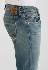 Lichtblauwe denim jeans met een vervaagde wassing. Bevat vijf zakken, oranje stiksel en een leren logo-label op de taille.