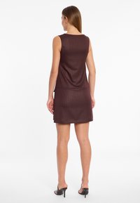 Bordeauxfarbenes ärmelloses Kleid mit einem taillierten Design, strukturiertem Stoff mit vertikalen Streifen und einem ausgestellten Saum, kombiniert mit schwarzen Plateausandalen.