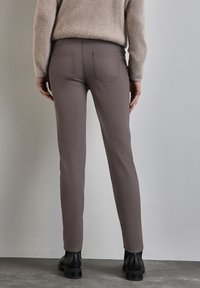 Fitted, hooggepaste, grijze broek van een gladde, rekbare stof; met achterzakken en een slanke pijpdesign. Gedragen met een beige sweater.