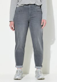 Jeans de mezclilla gris con un corte relajado, con dobladillos enrollados, bolsillos delanteros y una textura suave. Combinados con zapatillas gris claro.