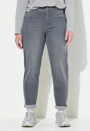 Jean en denim gris avec une coupe décontractée, présentant des ourlets roulés, des poches avant et une texture lisse. Associé à des baskets gris clair.