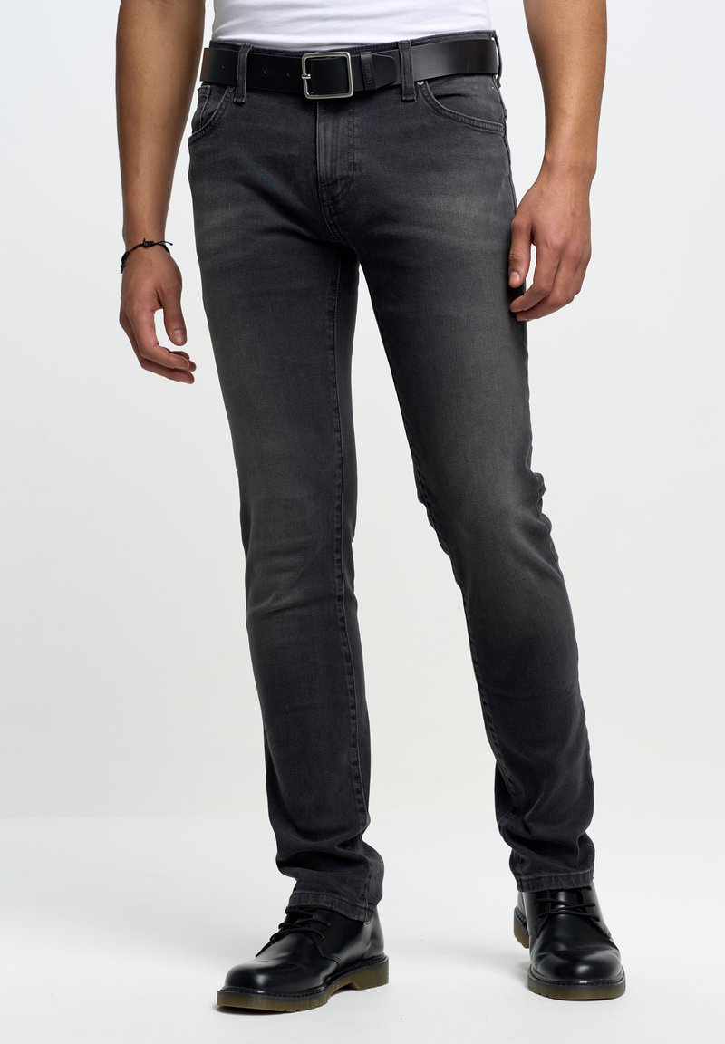 Jeans ajustados grises de mezclilla, con cinco pockets, pasadores para cinturón y un ligero desgastado. Combinados con botas de cuero negras con cordones.