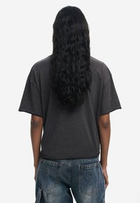 T-shirt gris surdimensionné avec un col rond et des manches courtes. Le tissu semble doux avec une texture légèrement décolorée. Porté avec un jean en denim bleu.