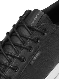 Black leather sneaker with textured surface, rounded toe, and lace-up design. Features a logo tag and contrasting white sole.
