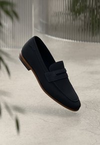 Ναυτικά δερμάτινα μοκασίνια με υφασμάτινη λωρίδα, στρογγυλή μύτη και ξύλινη σόλα, εμφανίζονται να αιωρούνται σε ουδέτερο φόντο.