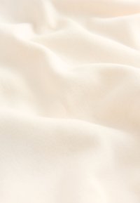 Tela de color blanco roto, suave y lisa, con pliegues delicados y una textura sutil, que sugiere un material acogedor y cómodo.