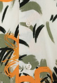 Hvidt stof med abstrakte grønne og sorte penselstræk samt orange blomster mønstre, prydet med to hvide fire-huls knapper syet lodret.