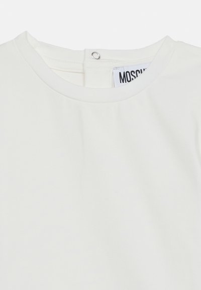 Vêtement blanc à col rond avec une fermeture par bouton-pression à l'arrière et une étiquette de marque partiellement visible à l'intérieur du col.