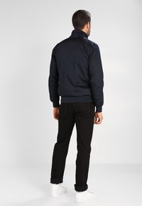 Marinblå bomberjacka med ståkrage, ribbade muddar och fåll, kombinerad med svarta jeans och vita sneakers. Mjukt tyg och elegant design.