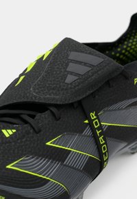 Black synthetic soccer cleat featuring textured upper, grey accents, and neon yellow detailing. Includes a lace-up design and padded tongue.