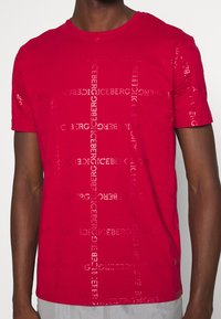 Rotes T-Shirt mit strukturiertem Design und wiederholtem "ICEBERG"-Logo, Rundhalsausschnitt, kurzen Ärmeln und normaler Passform. Aus weichem Baumwollstoff.