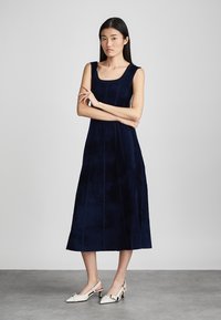 Ναυτικό μπλε, αμάνικο midi φόρεμα φτιαγμένο από μαλακό ύφασμα, με τετράγωνη λαιμόκοψη και κατακόρυφες ραφές, συνδυασμένο με κρεμ slingback παπούτσια.