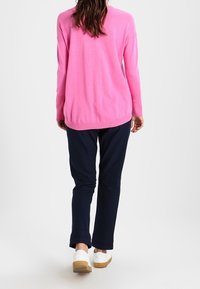 Roze gebreide trui met een losse pasvorm en verlaagde schouders, gecombineerd met marineblauwe broeken en witte sneakers, gezien vanuit de achterkant.