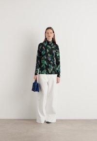 Bluză lungă, neagră, cu modele florale verzi și albastre, combinată cu pantaloni albi evazați și o geantă mică albastră.