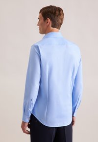 Camicia a maniche lunghe di colore azzurro chiaro, realizzata in un tessuto morbido; presenta un colletto classico, polsini con bottoni e un orlo curvo. Nessun motivo visibile.
