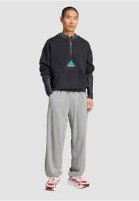 Čierna mikina na zips so tyrkysovým logom Adidas, šedé tepláciky a vzorované biele/červené tenisky. Textúrovaná látka; voľný strih.